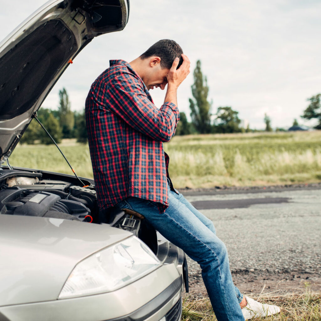 Man holding head sitting on car with car hood open