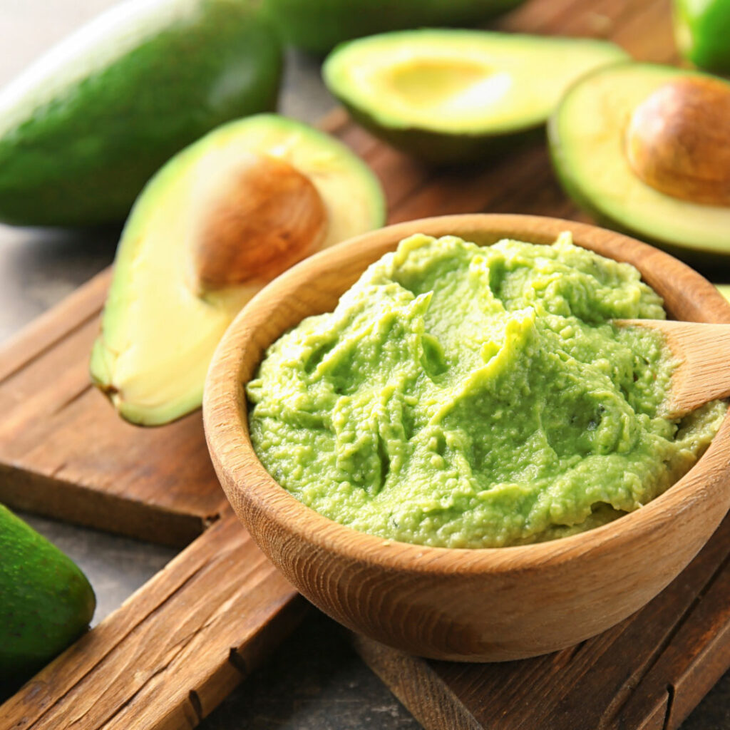 Guacamole in wooden bowl and wooden spoon. Surrounded by avocados