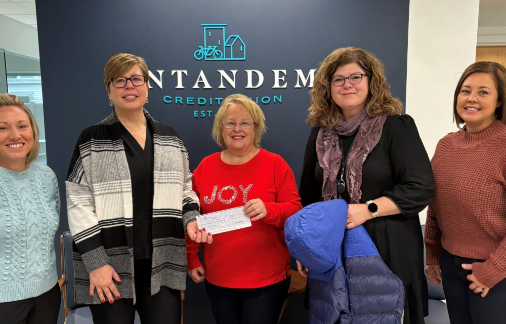 Intandem Credit Union leaders hand a donation check to Sherri, supporting her efforts to provide coats and winter gear to students in Grand Rapids.