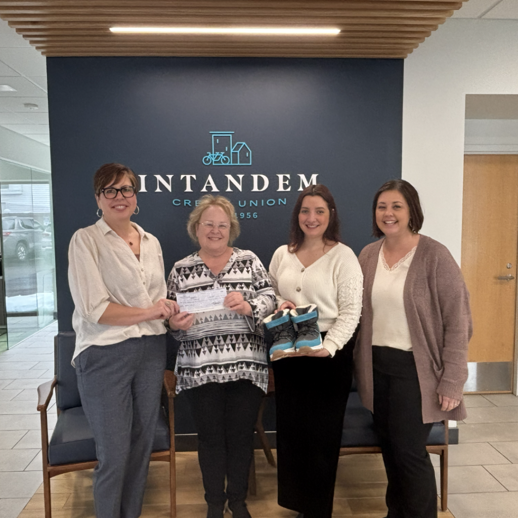 Intandem Credit Union leaders hand a donation check to Sherri, supporting her efforts to provide coats and winter gear to students in Grand Rapids.