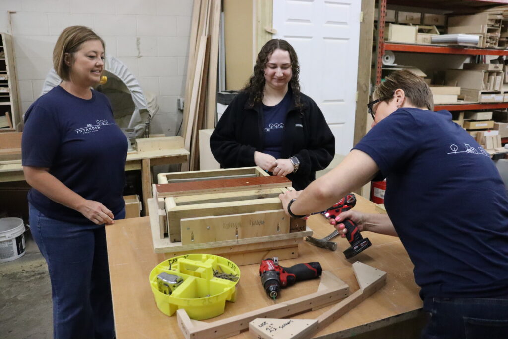 Team members using tools and assembling reclaimed wood tables while volunteering with Home Repair Services.