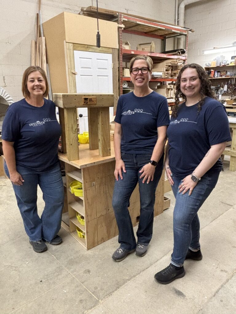 Intandem Credit Union team members posing with completed tables created from reclaimed materials during a volunteer day with Home Repair Services.